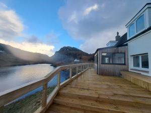 a house with a wooden deck next to a body of water at NC500 - Modern croft house at Handa in Scourie