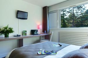 a hotel room with a bed and a desk and a window at Hotel Belambra Le Normont in Dourdan
