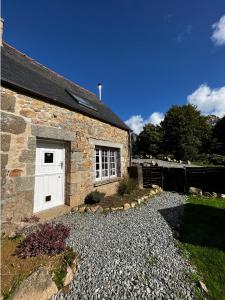 a stone house with a white door and a gravel driveway at L'Annexe in Maël-Pestivien
