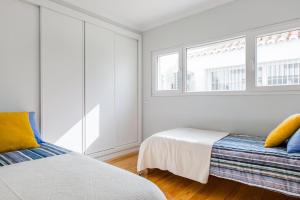 a white bedroom with two beds and two windows at Casa Alecrim in Tavira