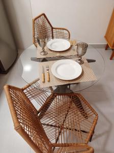 a glass table with two chairs and plates on it at Flat Canto dos Pássaros in Itacaré