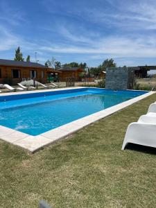 a large swimming pool with two white chairs in the grass at Complejo Anthea in Villa Yacanto