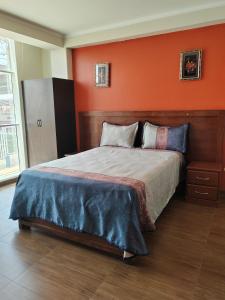 a bedroom with a bed with an orange wall at Hostal Bryan in Tacna