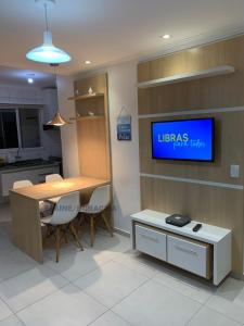 a kitchen with a table and a tv on a wall at Apto novo pertinho da praia em Boracéia, Bertioga in Bertioga