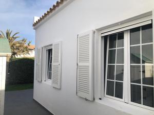 two windows with white shutters on a white house at Acogedora casa unifamiliar junto a la playa in Cala en Bosc