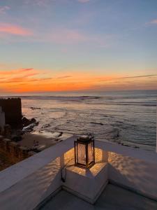 un coucher de soleil sur l'océan avec une lumière sur une corniche dans l'établissement Asilah * Dar Badiaa * Riad vue sur l’Atlantique, à Assilah
