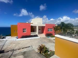 uma casa vermelha e amarela com o oceano ao fundo em La Vue de Basseterre Apartments - Luxury in Bird Rock em Basseterre