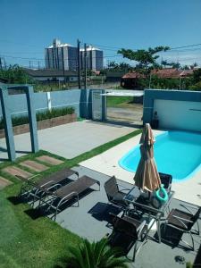 eine Terrasse mit Stühlen und einem Sonnenschirm neben einem Pool in der Unterkunft Casa alto padrão Matinhos in Matinhos