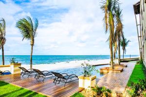 una terraza con tumbonas, palmeras y la playa en Varandas Do Mar Modern Deluxe Apartment Beach Front Cumbuco, en Cumbuco