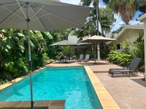 a swimming pool with an umbrella and chairs and tables at Talpa Tropix- 5 min stroll to beach in Palm Cove