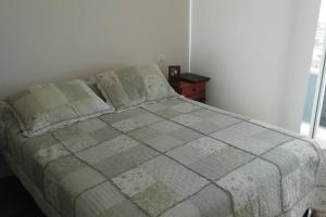 Cama en habitación blanca con colcha y almohadas en Acogedor Departamento en Concón, con piscina, en Concón