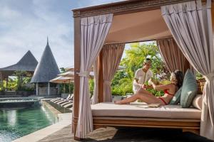mężczyzna i kobieta siedzący na łóżku obok basenu w obiekcie The Alena a Pramana Experience w mieście Ubud