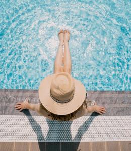 a woman in a hat sitting next to a swimming pool at Hotel Empire Albania in Durrës