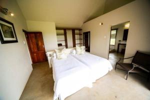 a bedroom with a large white bed and a chair at Bushwillow Lodge, Royal Jozini PGR, eSwatini in Lavumisa