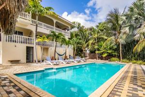 a swimming pool in front of a house with palm trees at Droom appartementen in Willemstad
