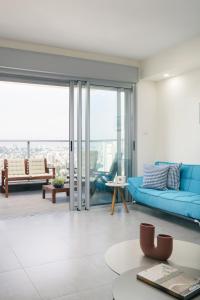 uma sala de estar com um sofá azul e portas de vidro em Deluxe & Terrace with City Overview by FeelHome em Holon