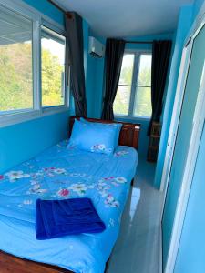 a bedroom with a bed with blue walls and windows at Twocans Resort KohMak - SHA in Ko Mak