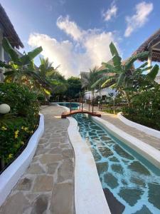 a swimming pool next to a resort with palm trees at Tembo House - Rafiki Village in Watamu