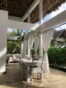a table and chairs on a patio with white curtains at Tembo House - Rafiki Village in Watamu