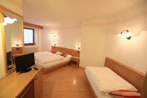 a hotel room with two beds and a desk with a television at Appartamenti Arnica in Alba di Canazei