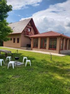 a building with a picnic table and white chairs in the grass at Számadó Vendégház in Poroszló
