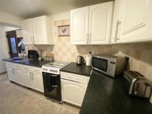 a kitchen with white cabinets and a microwave at Stunning 4-bedroom Cabin with Hot Tub in Beattock! in Beattock
