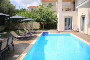a swimming pool with chairs and umbrellas next to a house at Amarianos Villas in Agia Effimia
