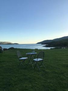 two chairs and a table in the grass near the water at Snowdonia Shepherds Hut + Hot Tub in Barmouth