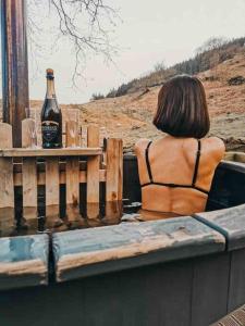 a woman sitting at a table with a bottle of beer at Ash Cabin with Hot Tub in Barmouth