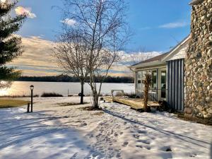 une maison avec des empreintes de pas dans la neige à côté d'un lac dans l'établissement Scenic & Serene Lakefront Cottage With Wood Stove, à Crivitz
