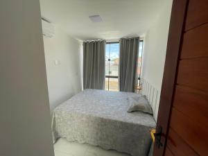 um pequeno quarto com uma cama e uma janela em Flats do Lucca em Tamandaré