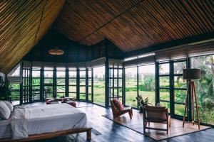 a bedroom with a bed in a room with windows at Let's Get Lost Ubud in Ubud
