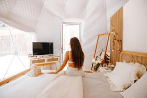 una mujer sentada en una cama mirando por la ventana en Romantic DOME with hot jacuzzi and Jungle view, en Klungkung