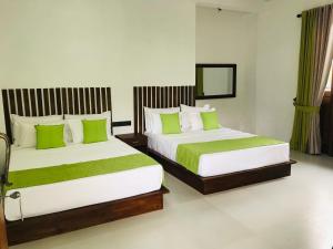 2 Betten in einem Hotelzimmer mit grünen Kissen in der Unterkunft Divine Villa in Anuradhapura