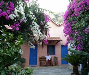 a woman sitting on a bench in front of a house with flowers at S West Crete Cottage in Palaiochóra