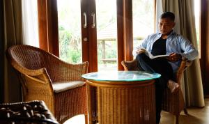 Villa & Farm for 5, near Sidemen w/ Mt. Agung View في Selat: رجل جالس على كرسي يقرا كتاب