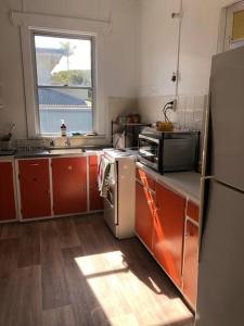 una cocina con armarios naranjas, fregadero y ventana en Sawtell cottage. 5min to beach.Pets, en Sawtell