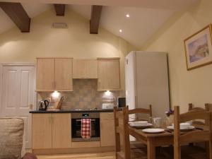 La cuisine est équipée d'une table, de chaises et d'un réfrigérateur. dans l'établissement Pinfold Holiday Cottage, à Laxey