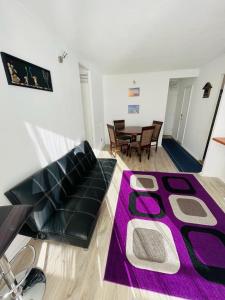 sala de estar con sofá negro y alfombra morada en Departamento Playa Bellavista, estacionamiento privado, vista al mar, 2 dormitorios 3 camas en Tomé