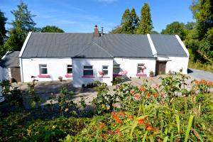 a white house with a black roof and some flowers at Corderry Farmhouse, idyllic cottage amid 250 acres in Stagdale Bridge