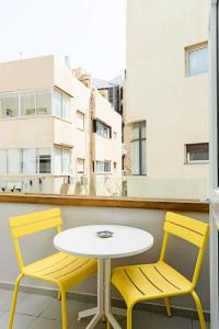 two yellow chairs and a white table on a balcony at Olive Gordon By The Beach in Tel Aviv