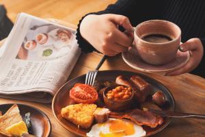 a person holding a cup of coffee next to a plate of breakfast food at The Old Success Inn in Sennen Cove
