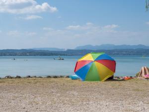 kolorowy parasol siedzący na plaży blisko wody w obiekcie Holiday Home San Francesco Camping Village by Interhome w mieście Rivoltella del Garda