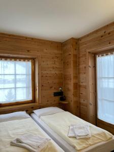 two beds in a room with wooden walls and windows at Bait Panorama in Livigno