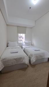 2 bedden in een witte kamer met een raam bij Lincoln Tower Podomoro Apartment in Medan