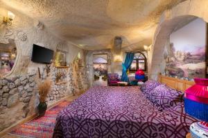 a living room with a purple bed and a stone wall at Cappadocia Splendid Cave Hotel in Ortahisar