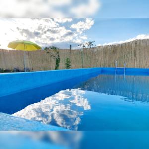 a blue swimming pool with an umbrella and a fence at Villa Emoción in Chilecito