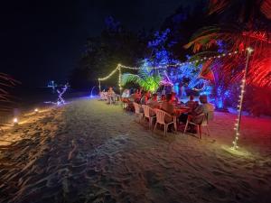 een groep mensen die 's nachts aan tafel op het strand zitten bij Coral Beach Maldives in Hangnaameedhoo