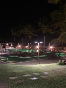 una piscina por la noche con palmeras y luces en Itacimirim vilage Villas da Praia en Itacimirim