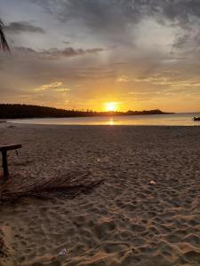 a sunset on a beach with a bench on the sand at Cabana Playa Cambiaso in San Felipe de Puerto Plata